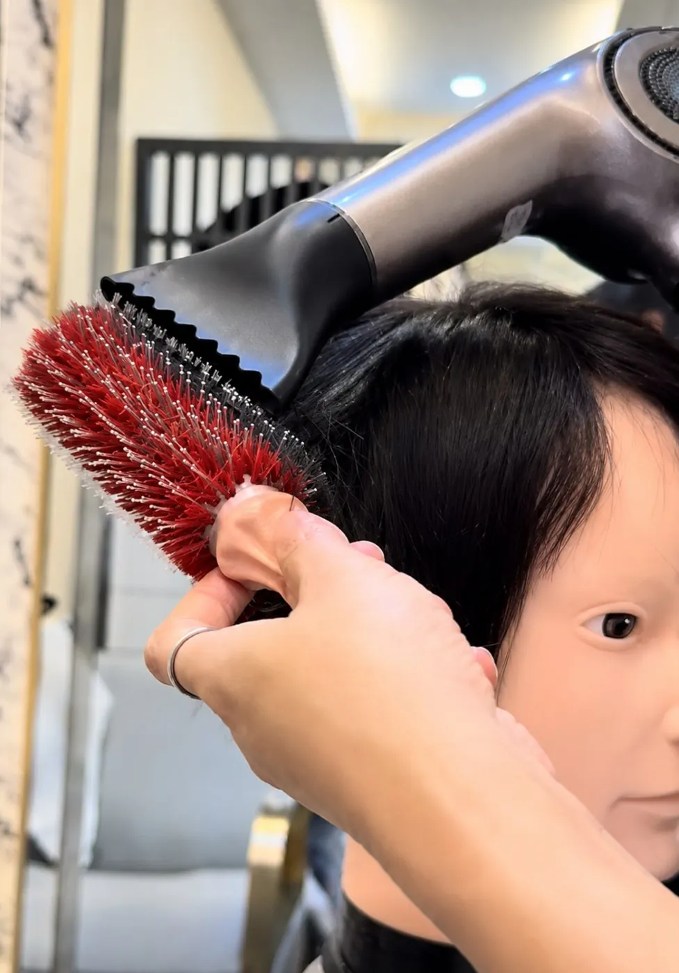 ช่างของร้านวิกผม Wewigs Pro กำลังเป่าแห้งและเซ็ตทรงวิกผมแท้บนหุ่นหัวด้วยแปรงกลม หลังเสร็จบริการซักและสปา